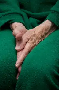 Old woman's hands tucked between her legs