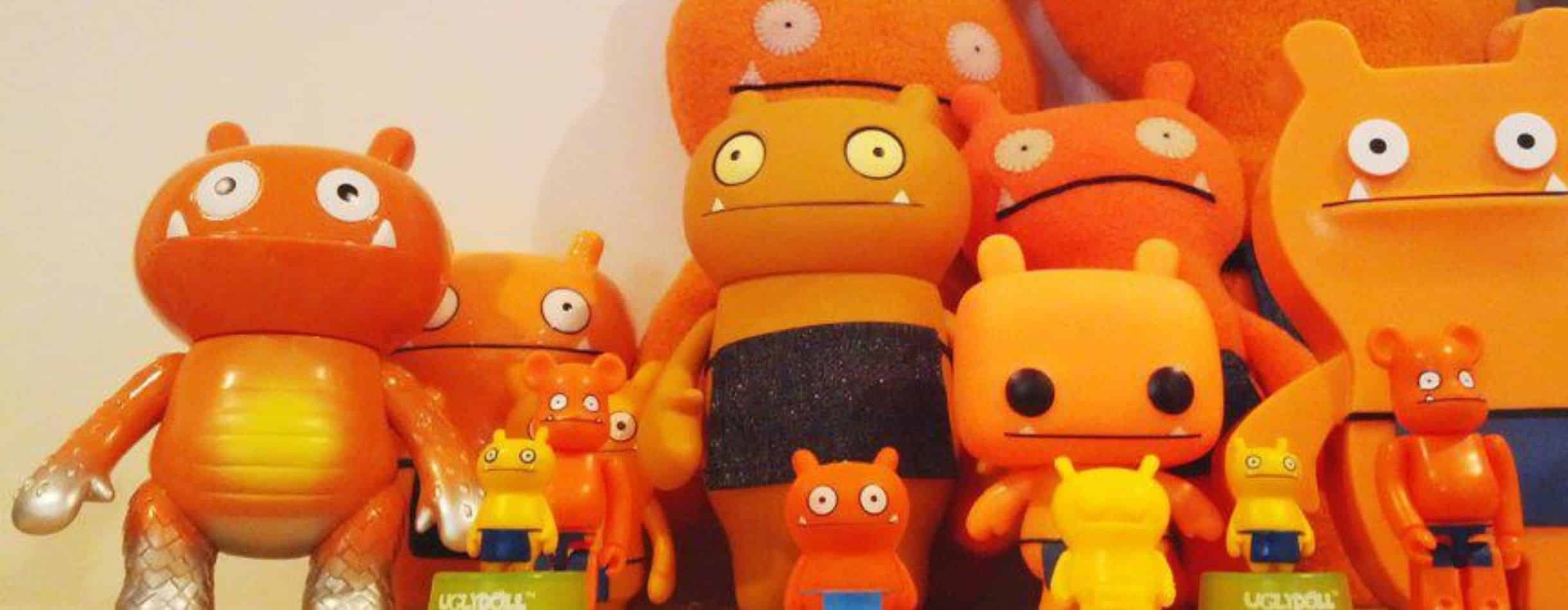 14 orange dolls sit on a shelf with unblinking eyes, awkward frowns, and a general unpleasantness to them.