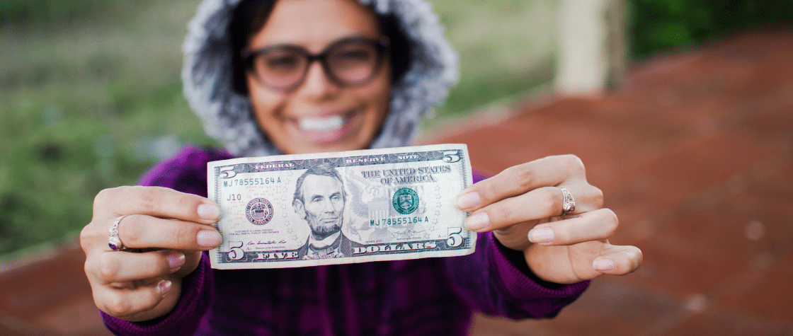 woman smiling while holding up a five dollar bill