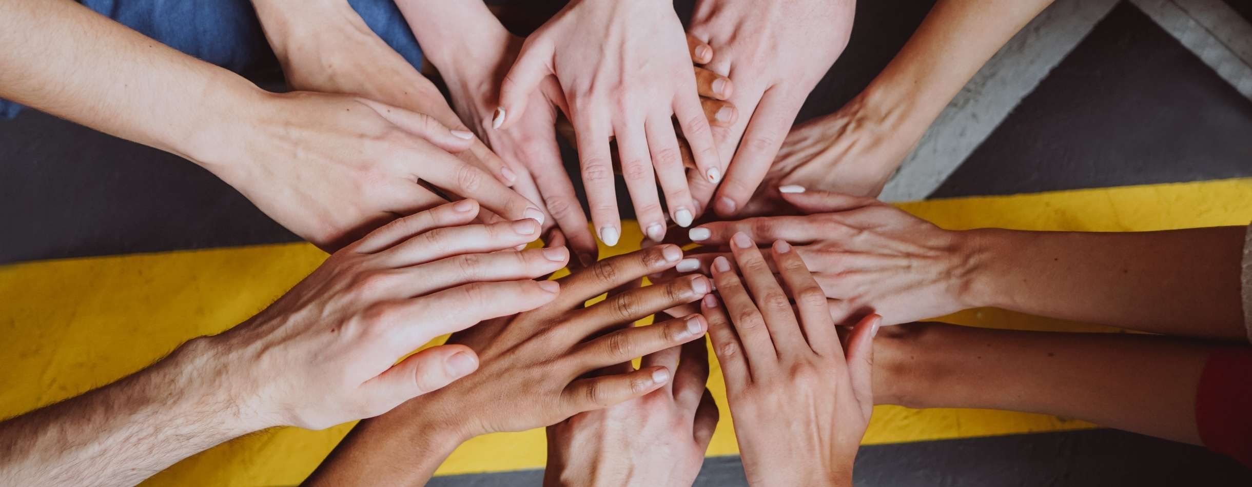 Several people place their hands on top of one another in a circle showcasing their camaraderie and strong team values.