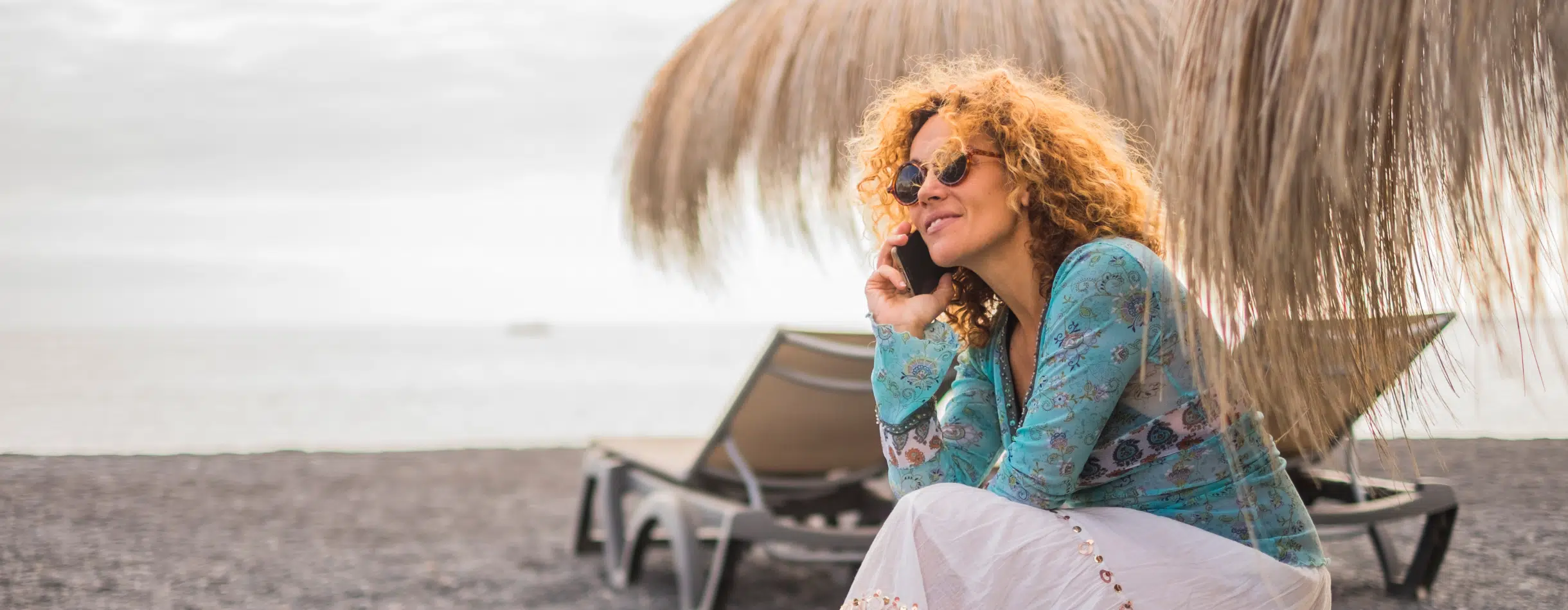 A woman on the beach gazes in the distance while listening attentively on the phone