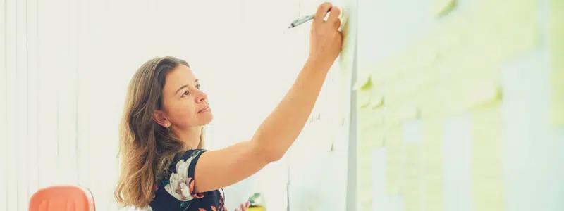 Women writing on whiteboard with sticky notes