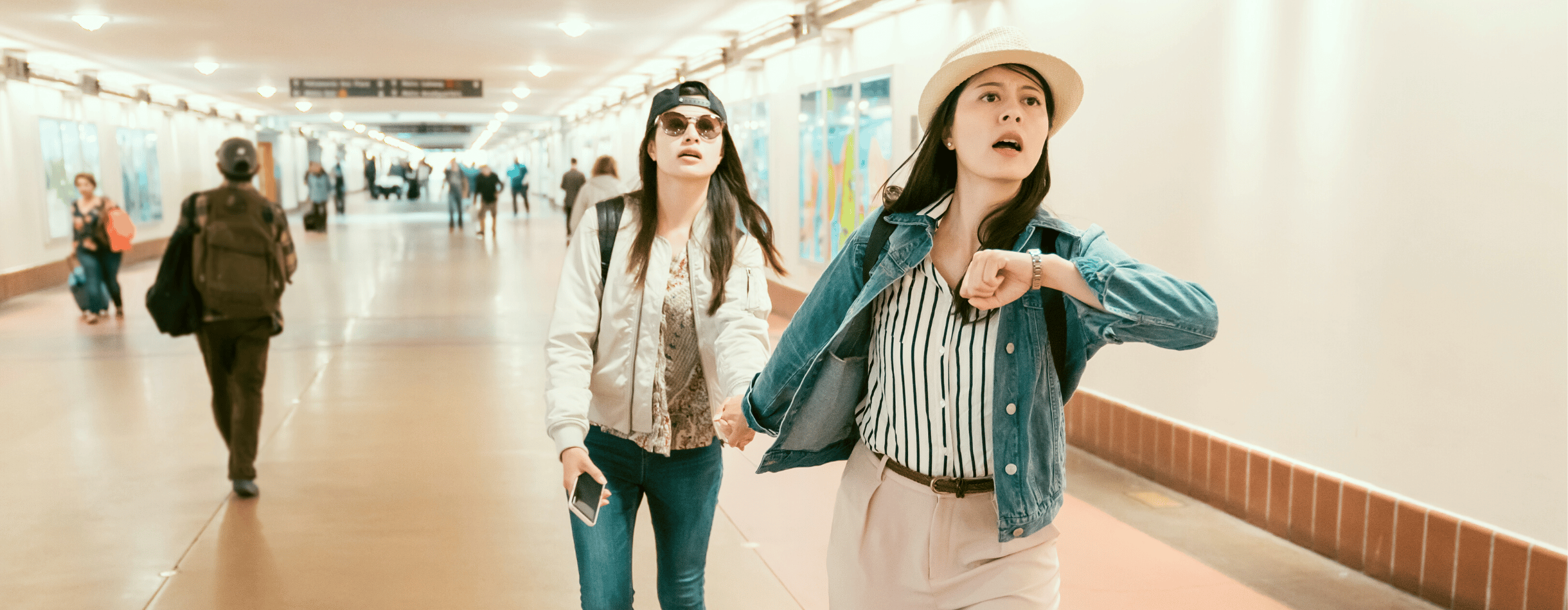 Two women are rushing to catch their flight on time. One of them is holding up her watch, likely using it to see how much time they have until their plane departs..