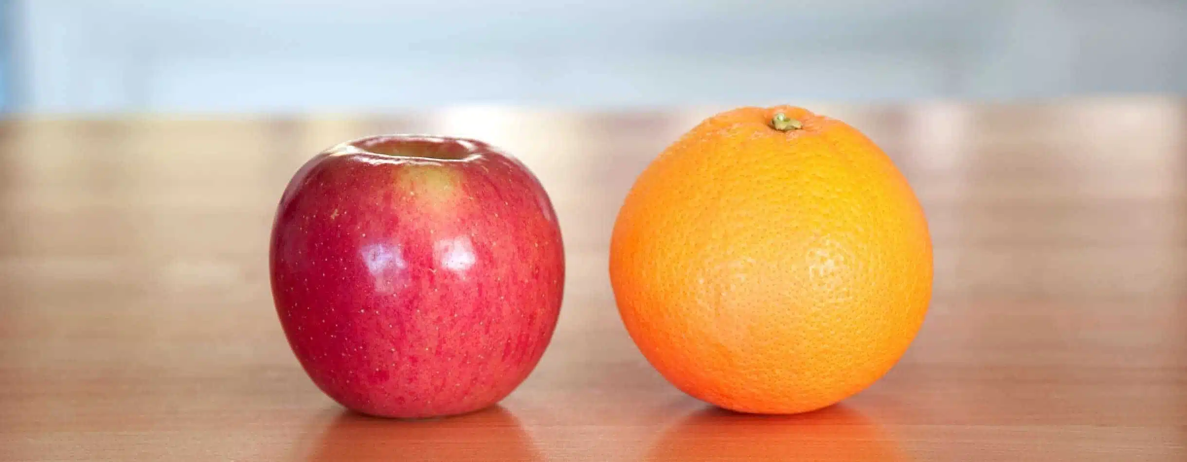 Apples to Oranges. A red apple and an orange lay next to one another on a table.