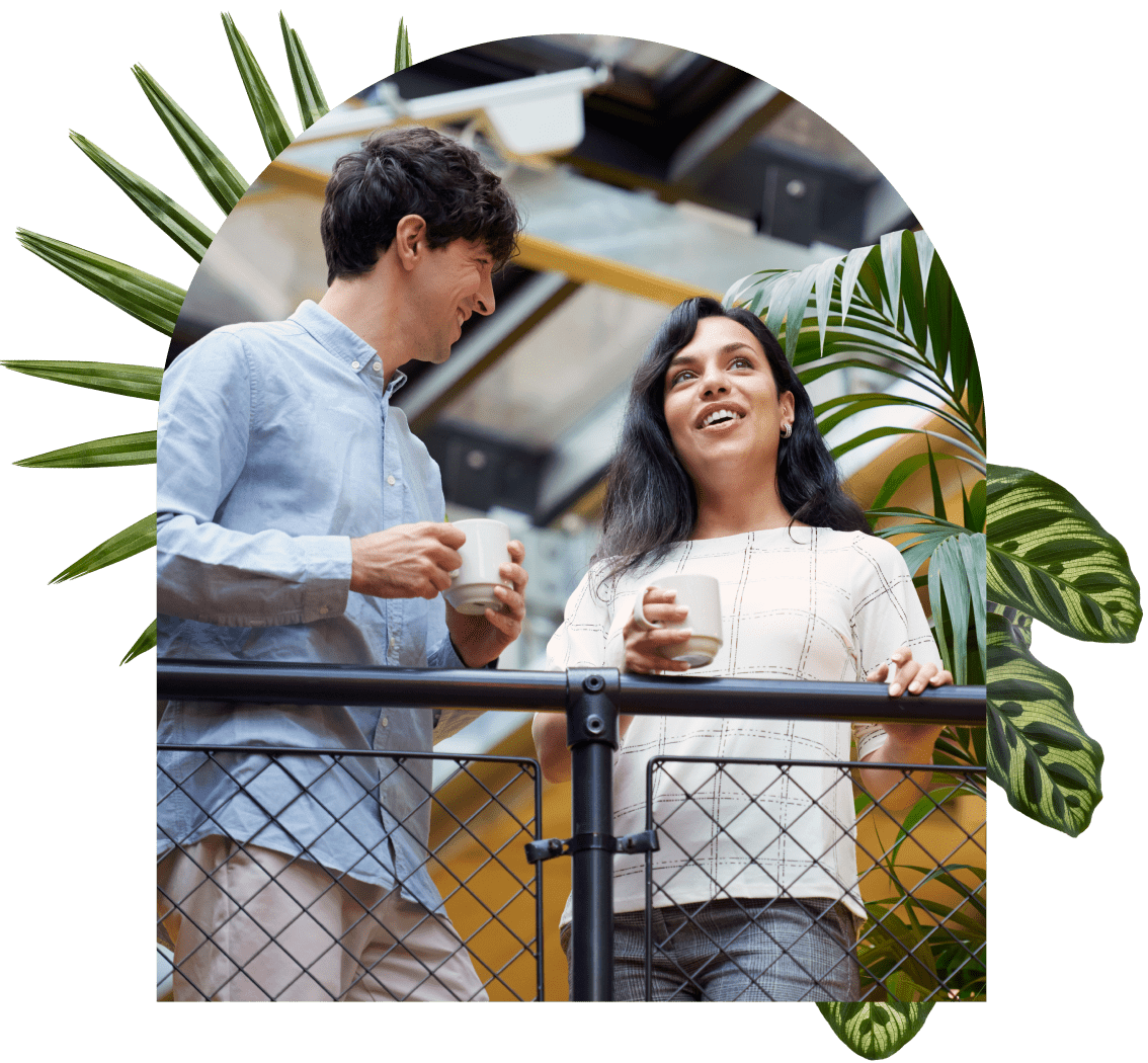 Two coworkers chat with coffee in hand overlooking their office.