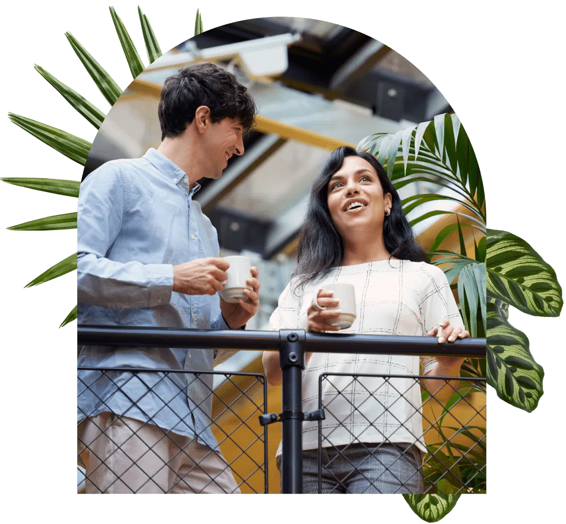 Two coworkers chat with coffee in hand overlooking their office.