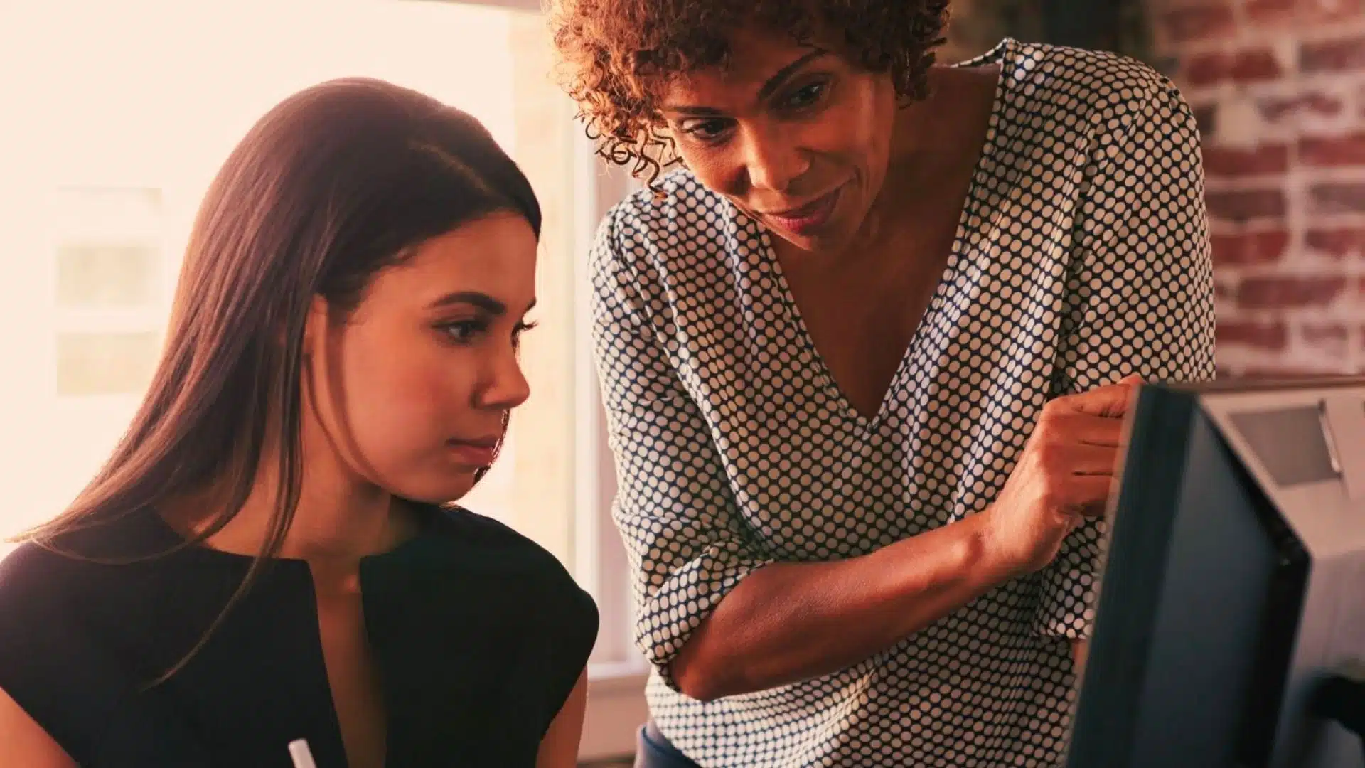 Woman helping a young girl work on a personal project on a computer