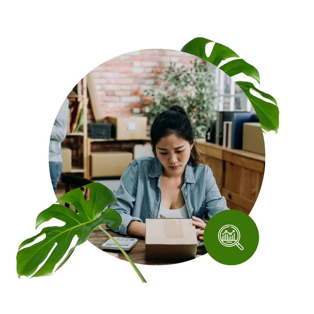 A woman in a denim jacket looks down at her laptop as she works through an assignment. Two monster leaves serve as secondary graphics to the image.