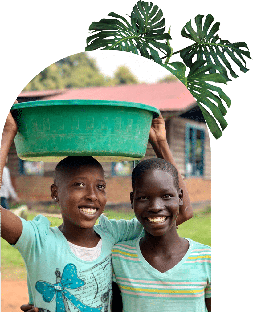Two young women smiling at the camera, carrying a bucket.